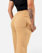 Tobe Hose Studio Damen Jogginghose in Beige mit Gesäßtasche und Markenlabel, getragen von einer Frau mit Tattoo