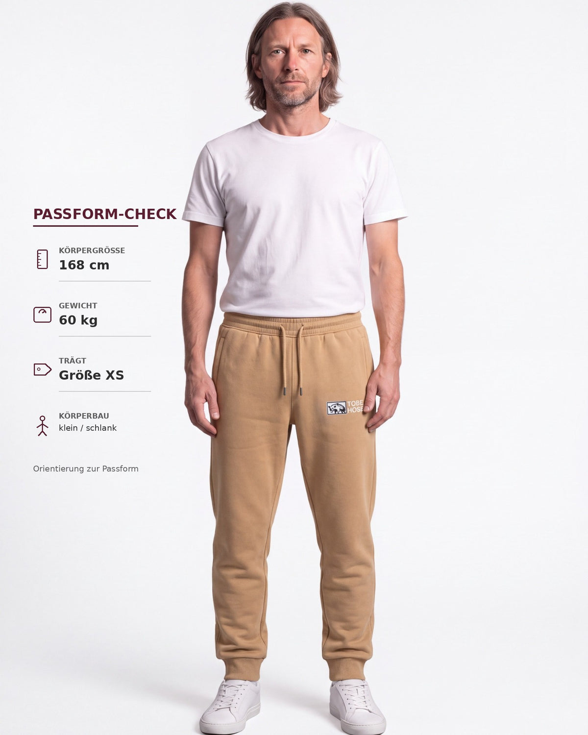 Tobe Hose Studio Jogginghose in Beige mit Hyänen-Logo-Stick, getragen von einem Mann mit weißem T-Shirt.