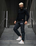 Tobe Hose Studio Herrenhose Luft in Schwarz aus robustem Nylon mit gesticktem Logo, getragen auf einer Treppe.