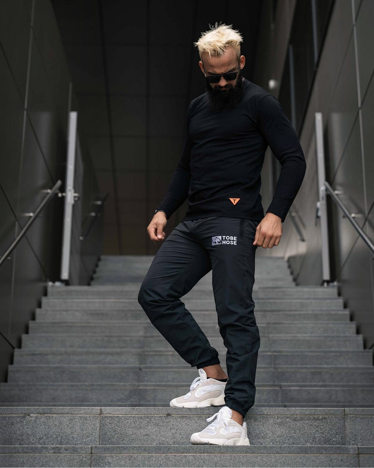 Tobe Hose Studio Herrenhose Luft in Schwarz aus robustem Polyester mit gesticktem Logo, getragen auf einer Treppe.