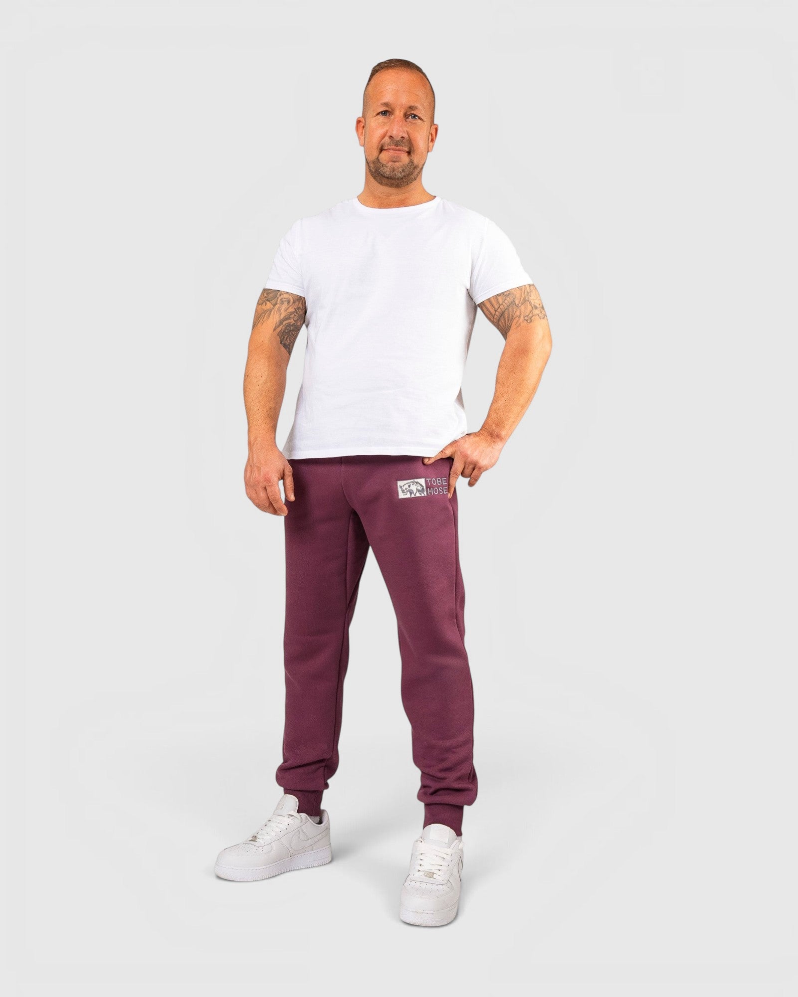Tobe Hose Studio Herrenhose in Pflaume mit elastischem Bund, Hyänen-Logo und Reißverschlusstaschen an einem Model
