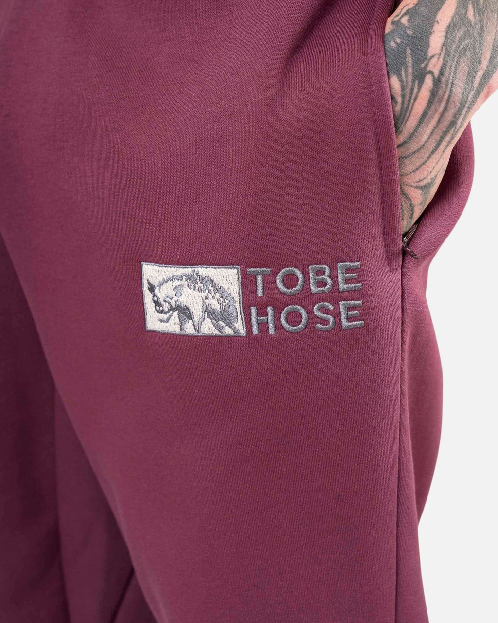 Tobe Hose Studio Herrenhose in Pflaume mit gesticktem Hyänen-Logo und praktischer Reißverschlusstasche