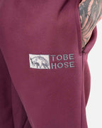 Tobe Hose Studio Herrenhose in Pflaume mit gesticktem Hyänen-Logo und praktischer Reißverschlusstasche