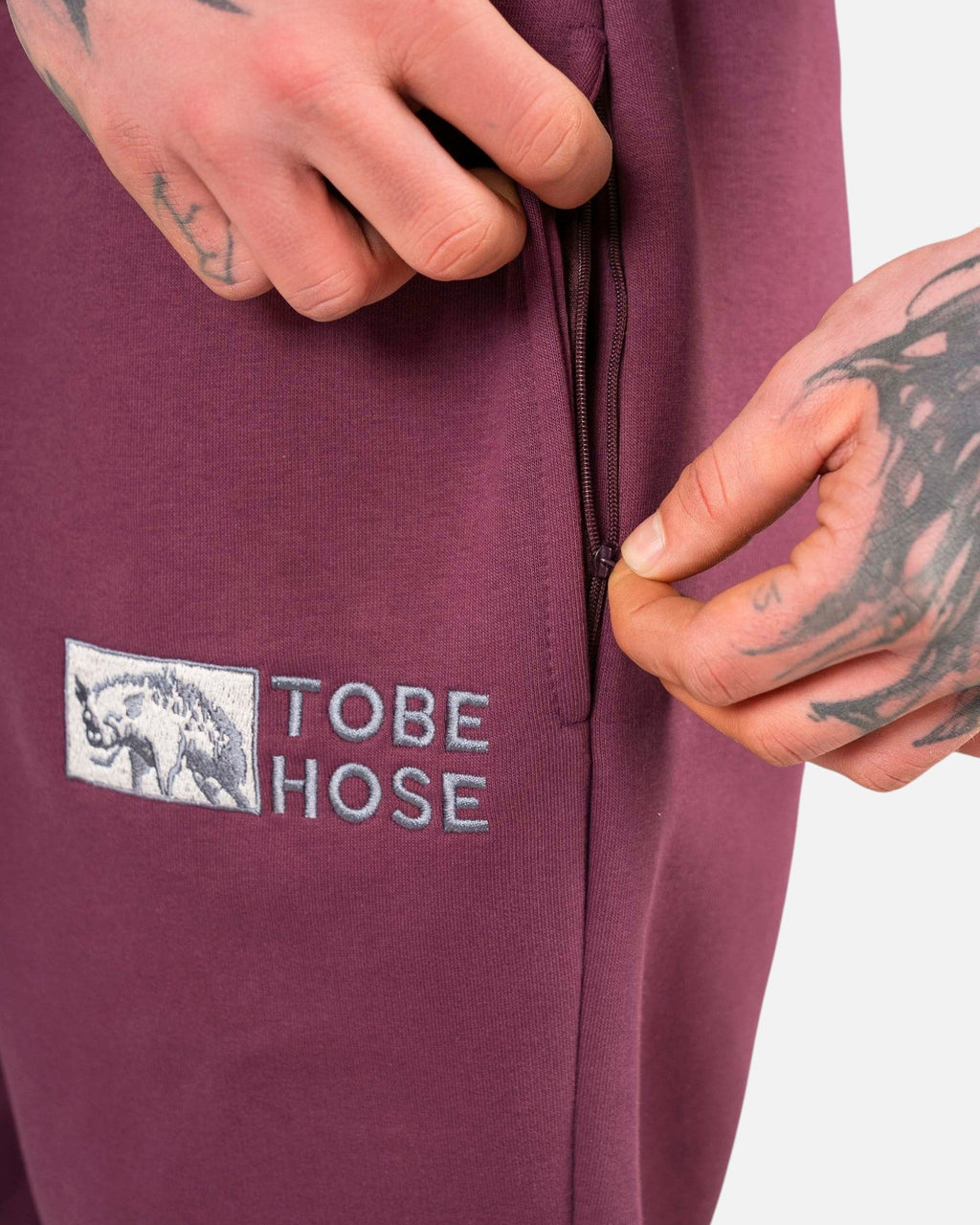 Tobe Hose Studio Herrenhose in Pflaume mit Reißverschlusstasche und gesticktem Hyänen-Logo auf robustem Stoff