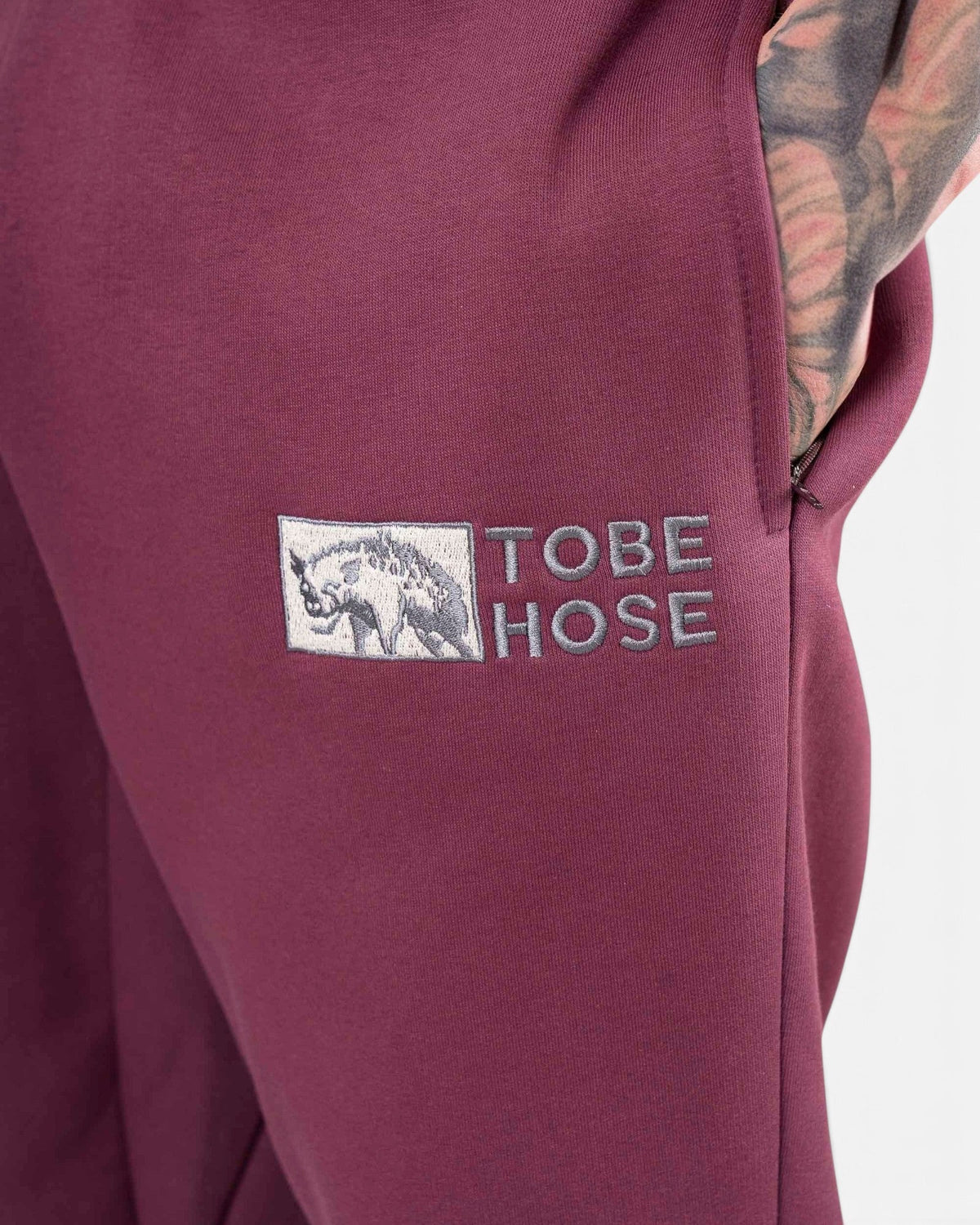 Tobe Hose Studio Herrenhose in Pflaume mit gesticktem Hyänen-Logo und praktischer Seitentasche mit Reißverschluss