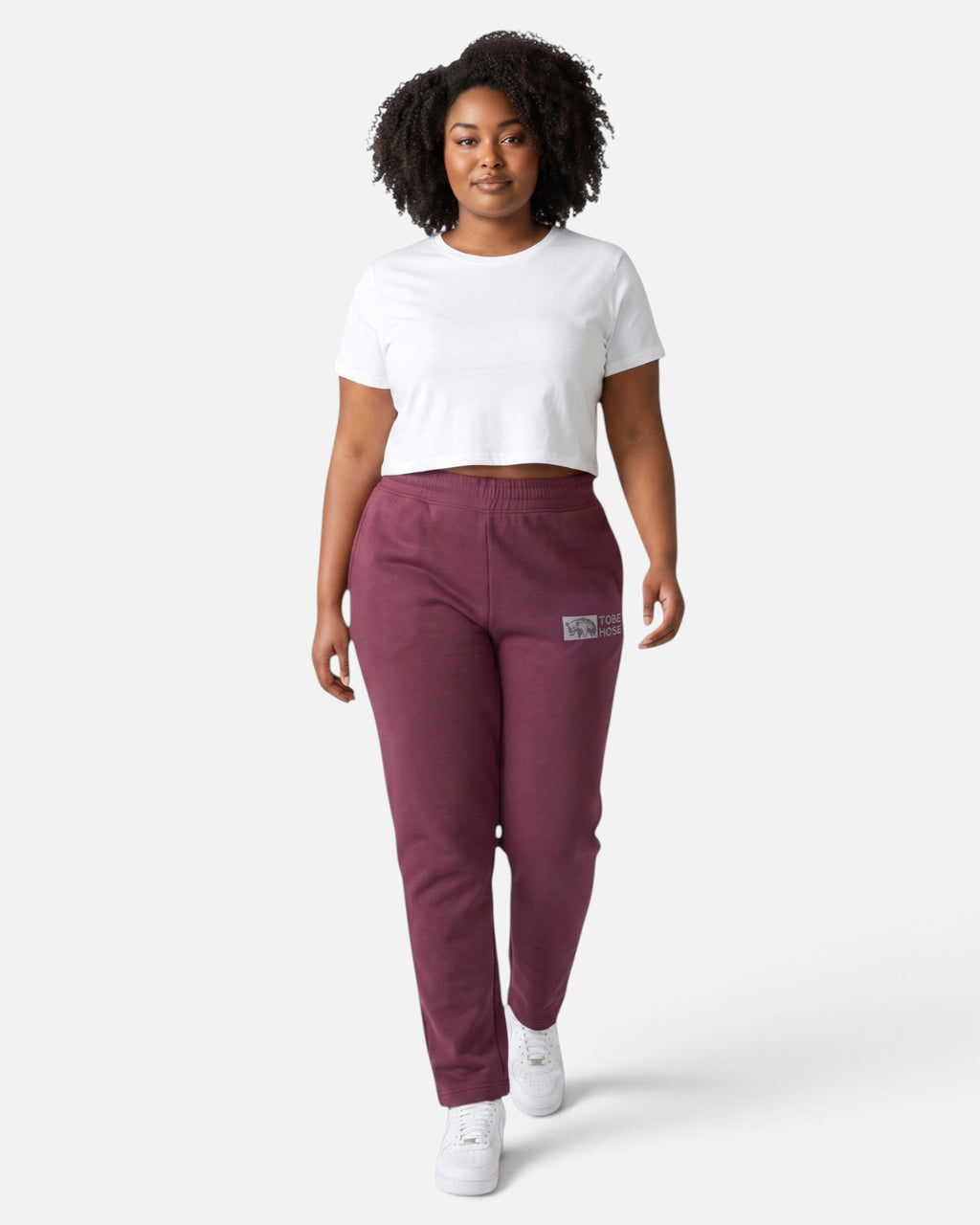 Model trägt Tobe Hose Studio Jogginghose in Pflaume mit Hyänen-Logo und Reißverschlusstaschen