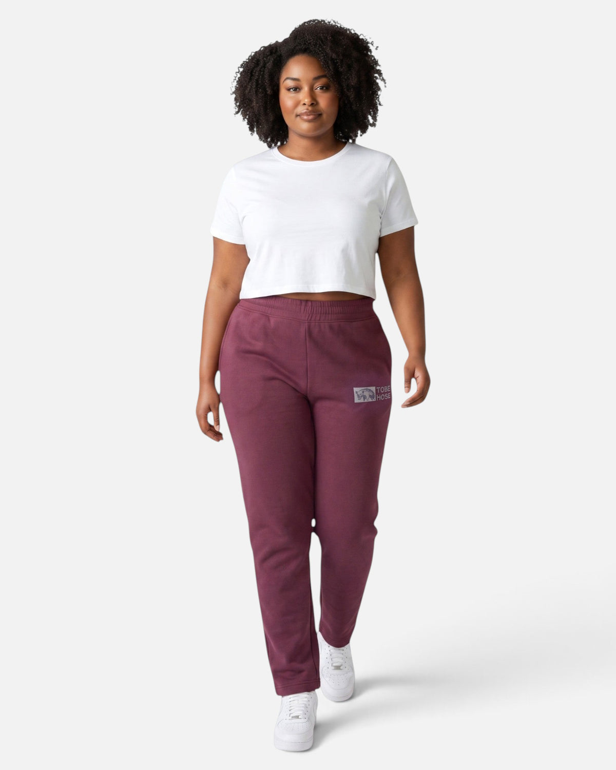 Model trägt Tobe Hose Studio Jogginghose in Pflaume mit Hyänen-Logo und Reißverschlusstaschen