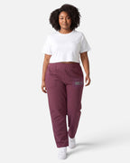 Model trägt Tobe Hose Studio Jogginghose in Pflaume mit Hyänen-Logo-Stick und Seitentaschen, kombiniert mit weißem Top.