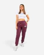 Model trägt Tobe Hose Studio Jogginghose in Pflaume mit elastischem Bund, Reißverschlusstaschen und Hyänen-Logo-Stick.