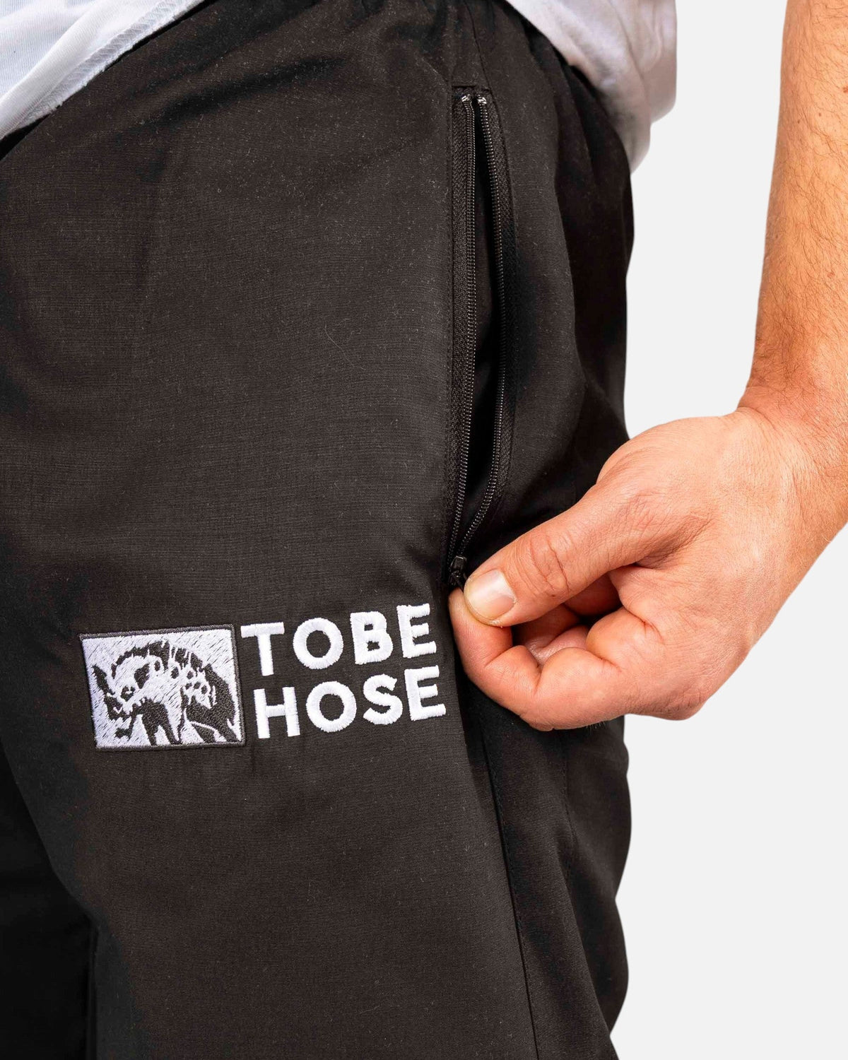 Tobe Hose Studio Herrenhose Luft aus robustem schwarzem Nylon mit Reißverschlusstasche und gesticktem Hyänen-Logo