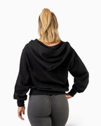 Tobe Hose Studio Zip-Hoodie Fels in Schwarz, Rückansicht an einer Frau mit Pferdeschwanz und grauer Leggings