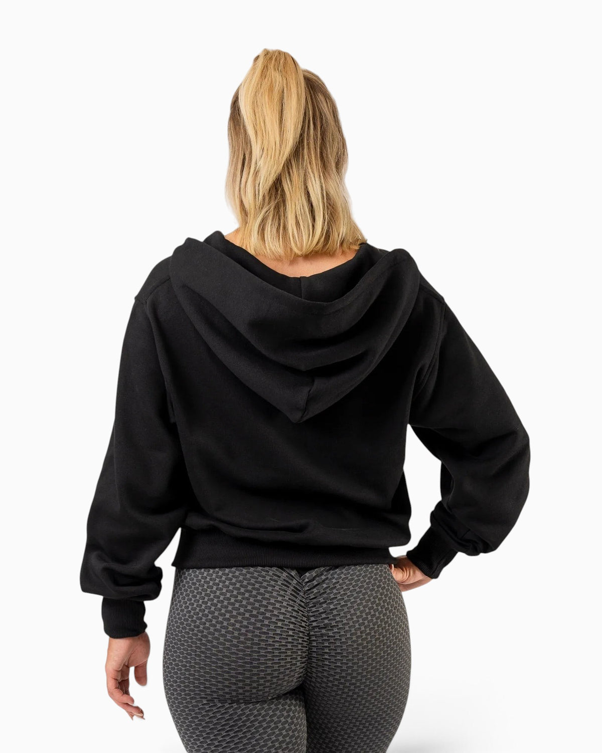 Tobe Hose Studio Zip-Hoodie Fels in Schwarz, Rückansicht an einer Frau mit Pferdeschwanz und grauer Leggings