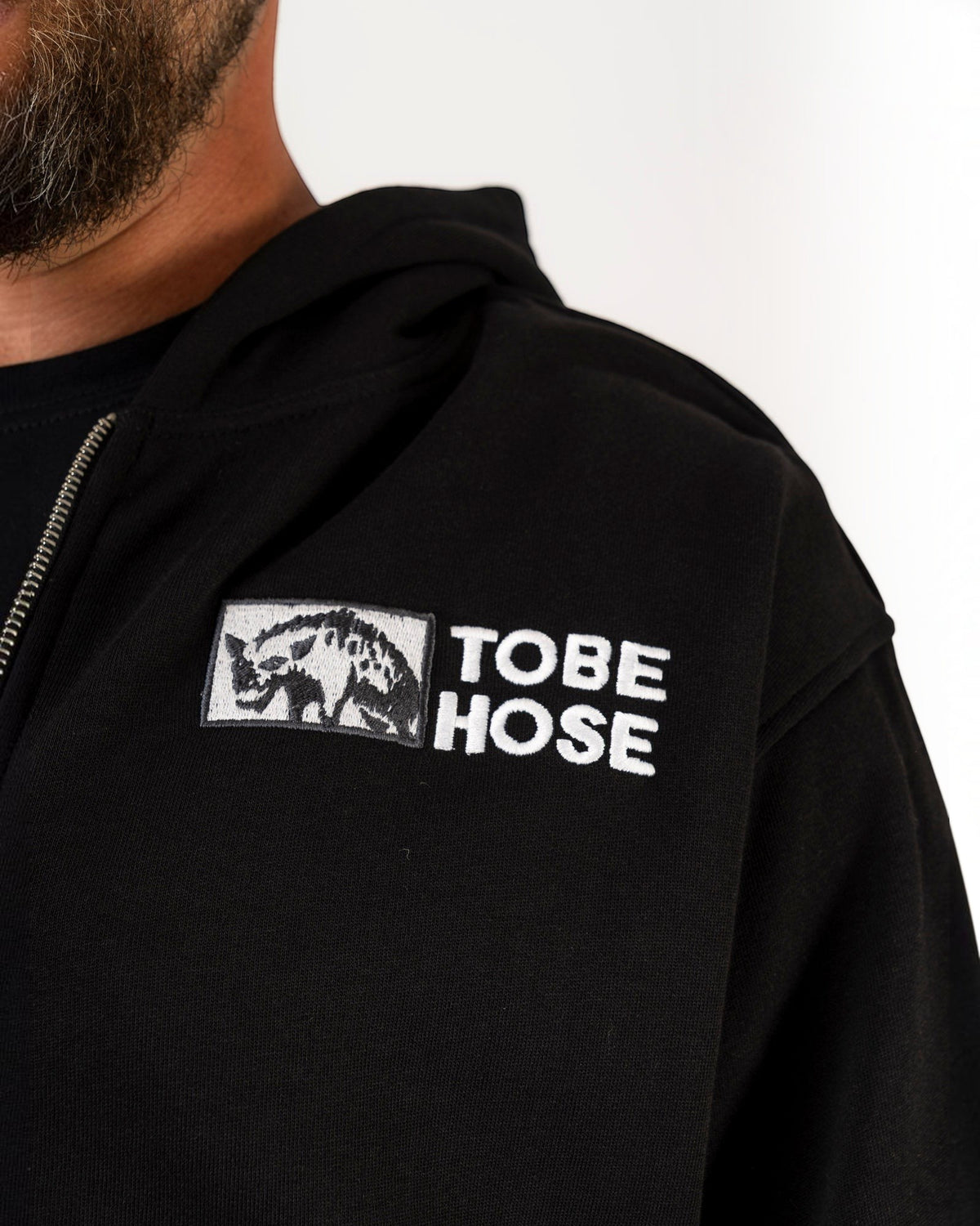 Tobe Hose Studio Zip-Hoodie Fels in Schwarz mit gesticktem Hyänen-Logo und Marken-Schriftzug auf der Brust